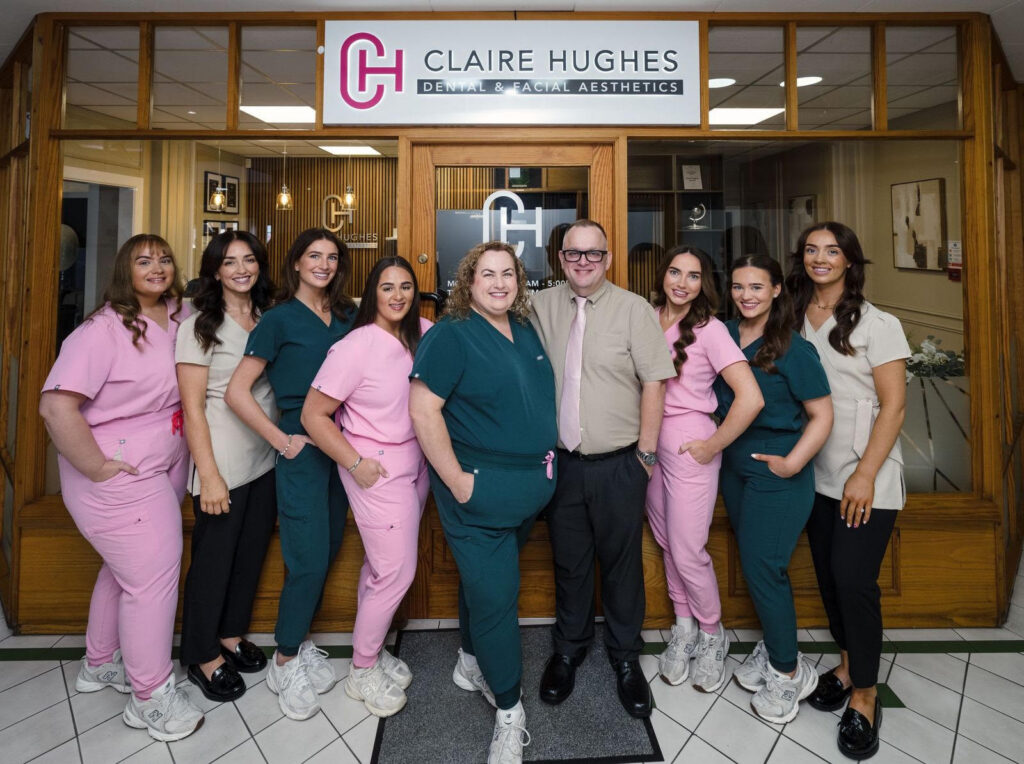 The team at Claire Hughes Dental & Facial Aesthetics, standing in a rpw outside the clinic's door and smiling